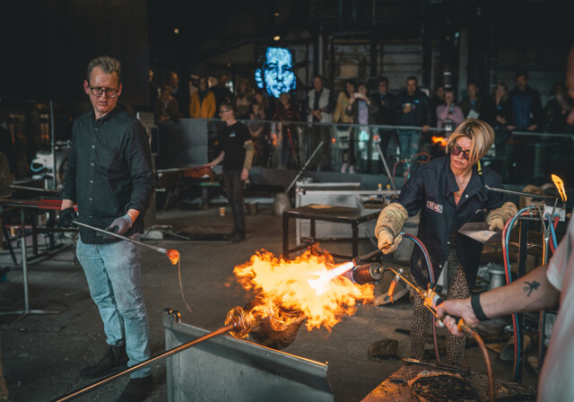 Frau und Mann produzieren mit Feuer das Glas im Holmegaard Vaerk Museum